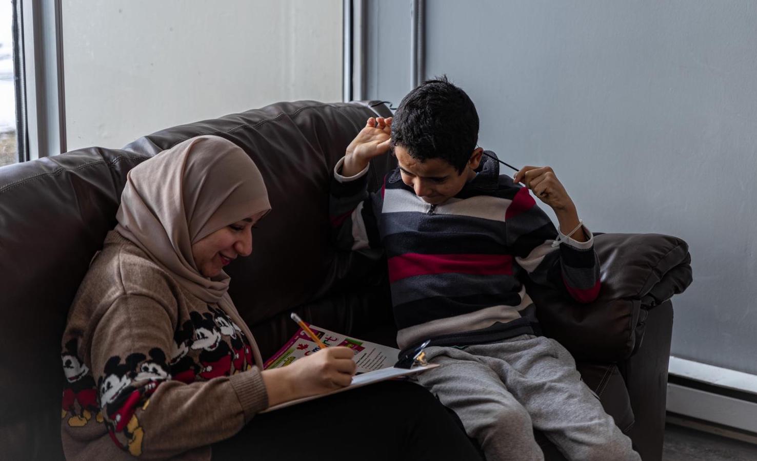 A mentor and child working in a notebook on a couch