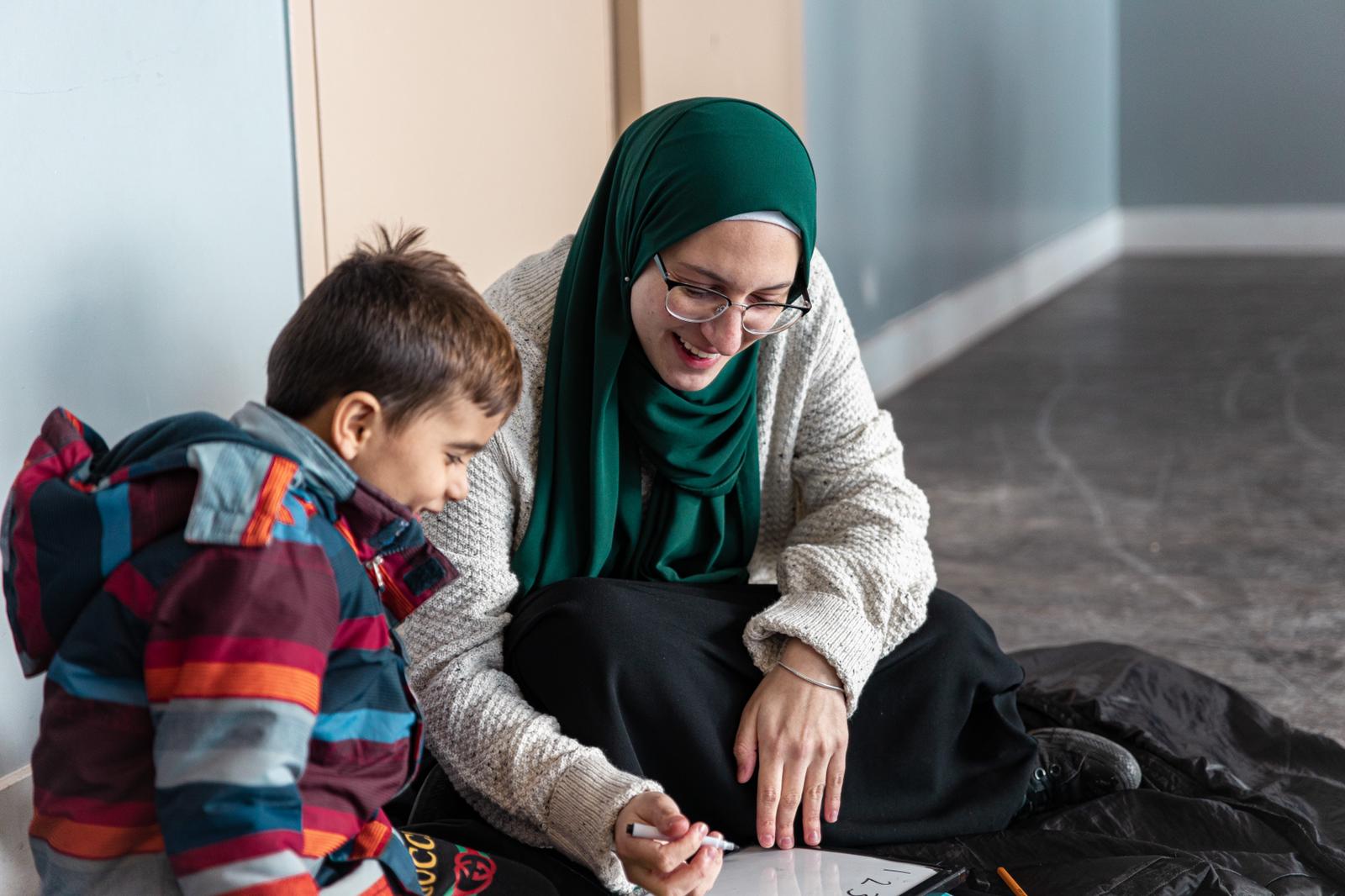 A mentor sitting on the floor, teaching a child on a whiteboard